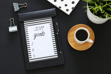 Top view 2019 goals list with notebook, cup of coffee over wooden black desk.