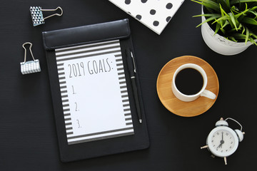 Top view 2019 goals list with notebook, cup of coffee over wooden black desk.