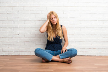 Fototapeta na wymiar Blonde girl sitting on the floor unhappy and frustrated with something. Negative facial expression on white brick wall background