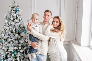 Fototapeta na wymiar Happy family Portrait In Home - father, pregnant mother and their little son. Happy new year. decorated Christmas tree. Christmas morning in bright living room.