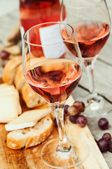 Two glasses of rose wine and board with fruits, bread and cheese on wooden table