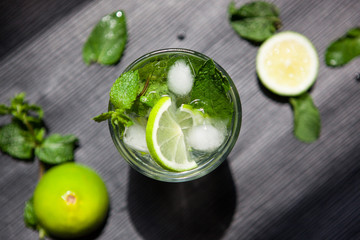 Mojito or fresh lemonade drink with lime and mint leaves on black table background, top view