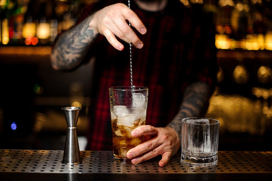 Barman stirring strong whiskey cocktail with ice cubes