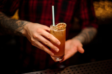 Bartender holding a glass of orange lemonade cocktail with a slice of fresh orange