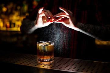 Barman splashing orange peel juice into a strong cocktail