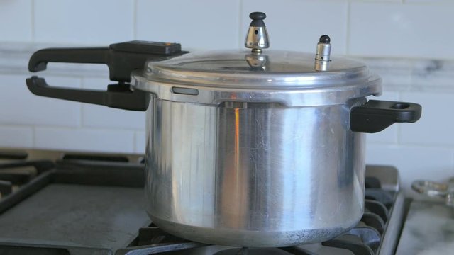 Pressure cooker pot releases pressure and steam while in the kitchen stove.