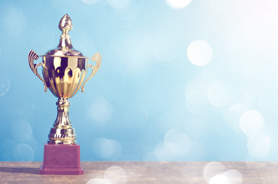 Golden winner's trophy on sky background standing on wooden desk festive bokeh blur background