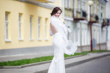 Naklejka premium young beautiful bride girl with wedding bouquet of roses stands on the street. the wind blows the veil