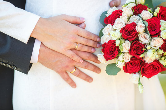 groom embraces the bride with wedding red white rose bouquet. rings on the hands of newly-married couple
