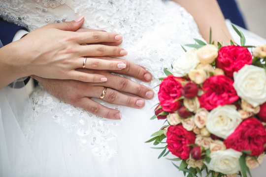 groom embraces the bride with wedding red white rose bouquet. rings on the hands of newly-married couple