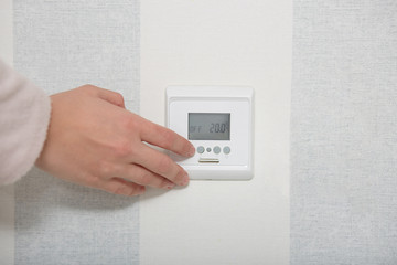 Smart home concept. Hands puches button switch on white wall, regulates temperature in flat or room. Close up, selective focus. Control panel © sementsova321