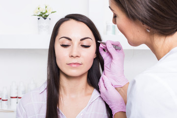 Beautician plucks a young woman's eyebrows with tweezers