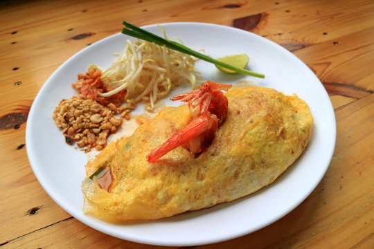 Thai Fried Noodle or Pad Thai Wrapped in Fried Egg Topped with Shrimps Served on Wooden Table