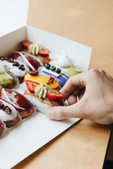Male hand taking delicious eclair with glaze, colorful dessert