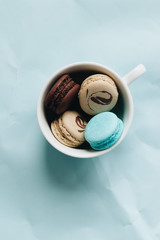 Composition of delicious macaroons in cup on blue table, sweet dessert