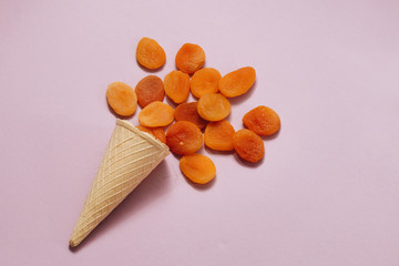 Crispy waffle cone with scattered dried apricots on purple background, food flat lay