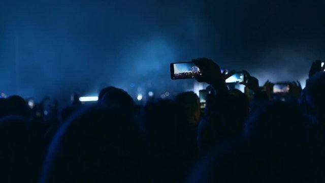 Lots of people with the smartphone turned on to record or take pictures during the live concert. Spectators at the concert photographed artist.