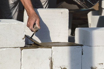 The bricklayer builds a brick wall and adds mortar to the trowel.
