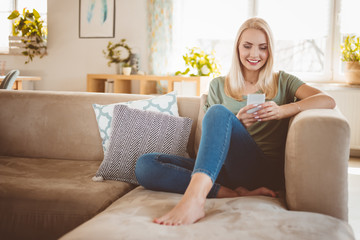 Young woman using smart phone on sofa in living room