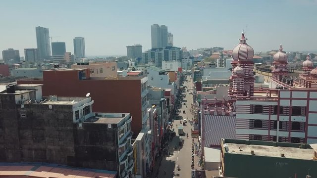 Aerial drone flying above a bustling street of Colombo, the capital city of Sri Lanka, towards the famous grand Red Mosque (Jami Ul-Alfar Mosque) with spectacular high rises on the skyline in the sun