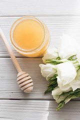 Honey dipper, honey and white flowers on wooden board
