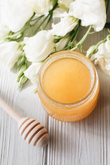 Honey dipper, honey and white flowers on wooden board