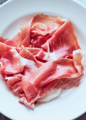Fresh organic italian meat prosciutto in a white plate top view