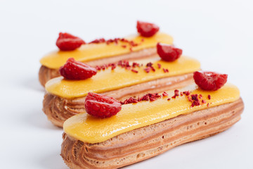 Set of delicious eclairs with yellow glaze and raspberries	