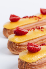 Set of delicious eclairs with yellow glaze and raspberries	