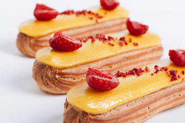 Set of delicious eclairs with yellow glaze and raspberries	