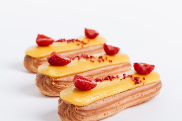 Set of delicious eclairs with yellow glaze and raspberries	