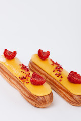 Set of delicious eclairs with yellow glaze and raspberries