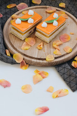 Two pieces of delicious cake on wooden board decorated with floral petals
