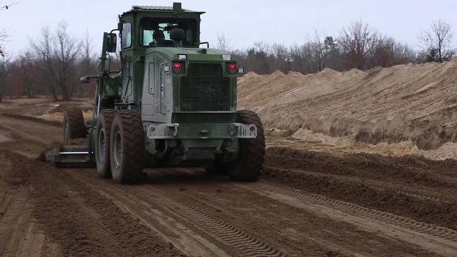 Military road grader leveling ground