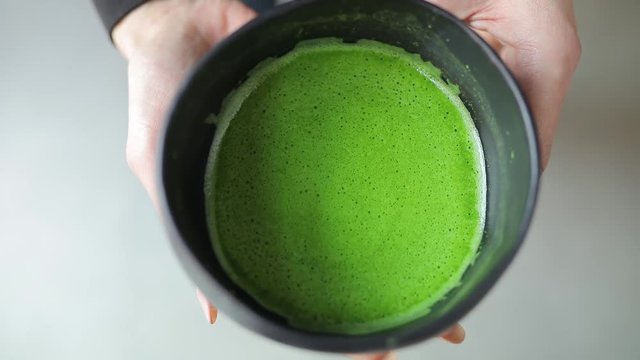 Matcha tea in bowl, top view of green drink in female hands