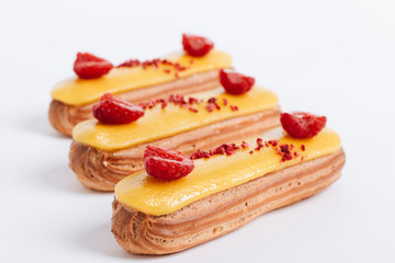 Set of delicious eclairs with yellow glaze and raspberries