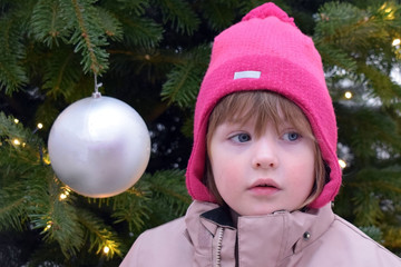 The girl in the hat stands on the background of the Christmas tree. The girl thoughtfully looks to the side against the backdrop of New Year's scenery.