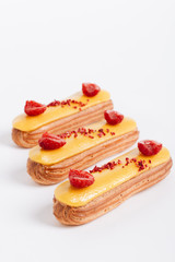 Set of delicious eclairs with yellow glaze and raspberries