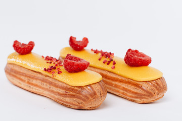 Set of delicious eclairs with yellow glaze and raspberries