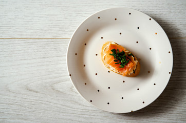 plate with a mini sandwich or tapas with salmon cheese and chives on a light wooden table