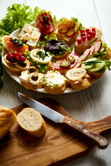 plate of colorful and healthy sandwiches or tapas with a knife and a baguette on a light wooden table