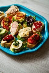 old blue tray with a set of healthy tapas or mini sandwiches on a light wooden table