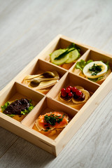 box with a set of healthy colorful mini sandwiches or tapas with vegetables and fish on a light table