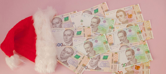 Ukrainian hryvnia banknotes coming out of Santa Claus hat on a pink background. Christmas Shopping Concept