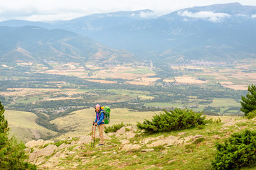 Fototapeta premium Woman hiker with big backpack stands on the rock and enjoys the valley view in Spanish Pyrenees mountains