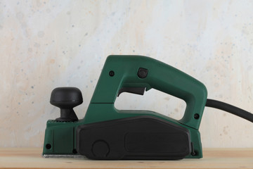 Electric planer on wooden table and against the background of a plastered wall.