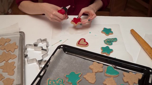 Girl decorates homemade gingerbread cookies with colored glaze close up. Christmas baking.