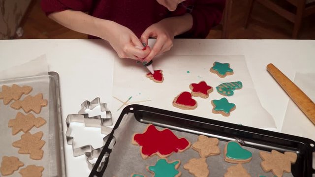 Girl decorates homemade gingerbread cookies with colored glaze close up. Christmas baking.