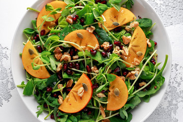 Persimmon and pea shoot salad with walnuts, pomegranate and pumpkin seed in a white table