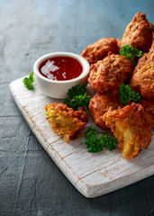 Crispy onion bhajis with sweet chilli sauce on white wooden board